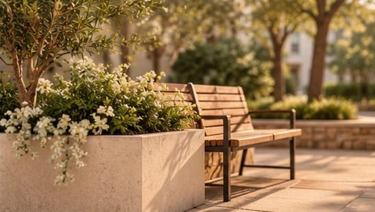 Un banc de bois à côté d'une jardinière en pierre fleurie de blanc, dans la lumière chaude du soir